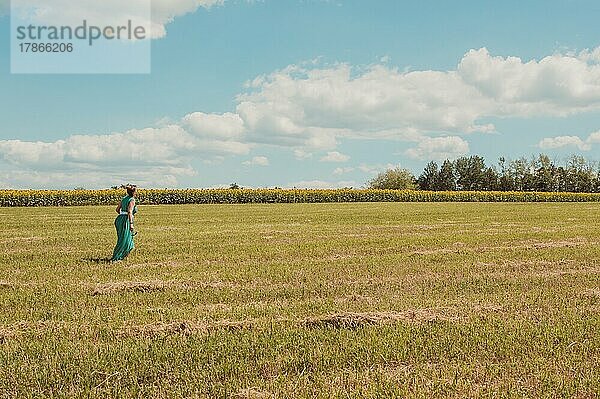 Frau in Grün geht durch sommerlich sonniges Feld