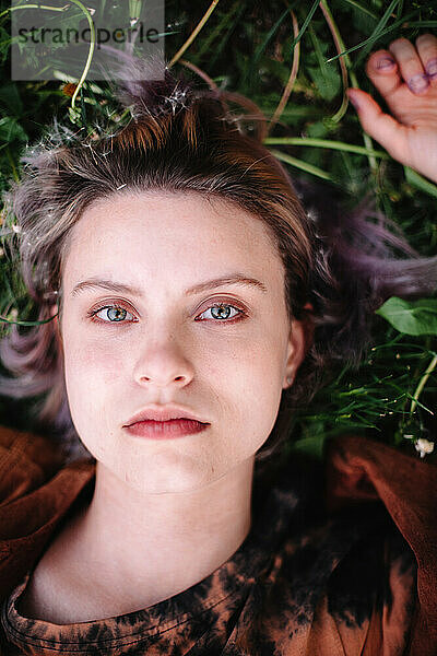 Porträt einer ernsthaften jungen Frau  die im Gras liegt und in die Kamera blickt