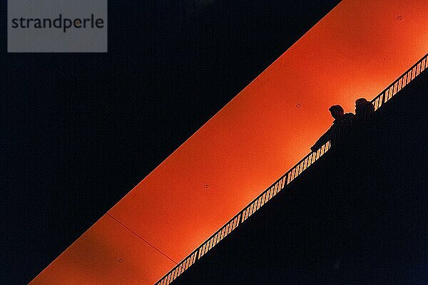 Zwei Personen  Paar steht auf Aussichtsplattform Plaza  genießt Aussicht  Silhouetten in der Dunkelheit  orange beleuchtet  Elbphilharmonie am Abend  Blick von unten  Textfreiraum  Hamburg  Deutschland  Europa