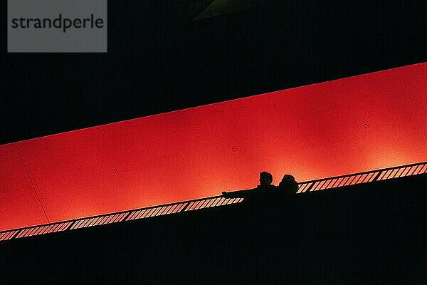 Zwei Personen  Paar steht auf Aussichtsplattform Plaza  schaut nach unten  Silhouetten in der Dunkelheit  orange beleuchtet  Elbphilharmonie am Abend  Blick von unten  Textfreiraum  Hamburg  Deutschland  Europa