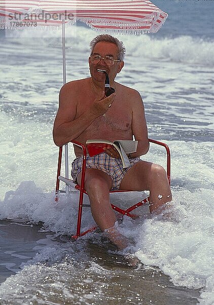 Älterer Mann mit Sonnenstuhl und Sonnenschirm am Meer  Strand  mit Pfeife rauchend  Urlaub  Erholung  Meereswellen  Older man with solar chair and sunshade by the sea  beach  with whistle smoking  vacation  rest  sea waves