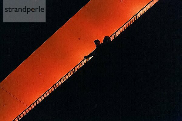 Zwei Personen  Paar steht auf Aussichtsplattform Plaza  genießt Aussicht  Silhouetten in der Dunkelheit  orange beleuchtet  Elbphilharmonie am Abend  Blick von unten  Textfreiraum  Hamburg  Deutschland  Europa
