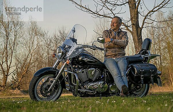 Glücklicher Mann im mittleren Alter  lehnt sich fröhlich und zufrieden an sein Motorrad  Karlsruhe  Deutschland  Europa