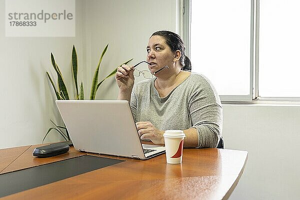 Reife Geschäftsfrau  die am Kopfende des Tisches in einem Bürobesprechungsraum sitzt  an ihrem Computer arbeitet und in Gedanken versunken ist