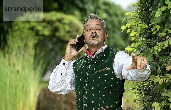 Mann mit Telefon in Bayrischer Tracht an einer Hecke  Karlsruhe  Deutschland  Europa