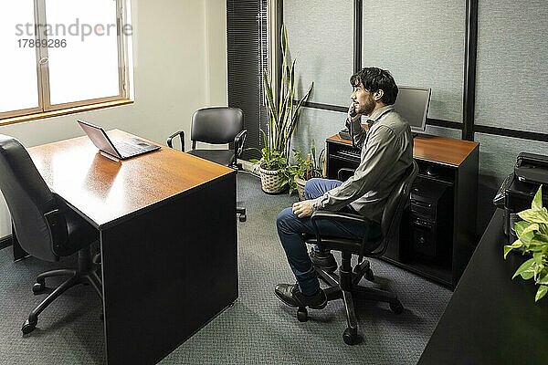 Geschäftsmann sitzt in seinem Büro und telefoniert  während er nachdenklich aus dem Fenster schaut