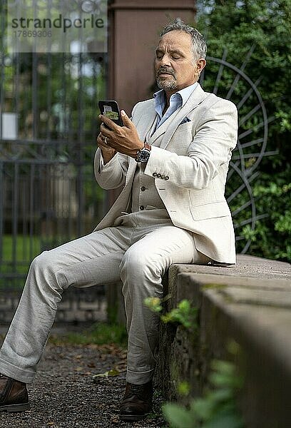 Mann im Anzug sitzt auf eine Mauer und schaut angestrengt in sein Telefon  Karlsruhe  Deutschland  Europa