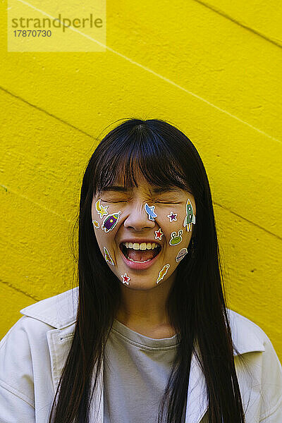 Happy young woman with stickers on face in front of wall
