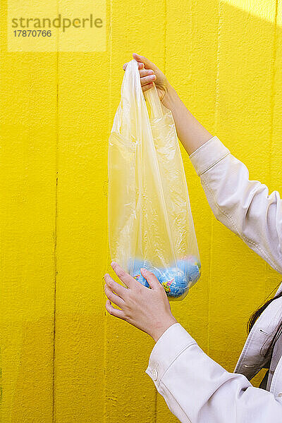 Junge Frau hält Globen in einer Plastiktüte vor einer gelben Wand