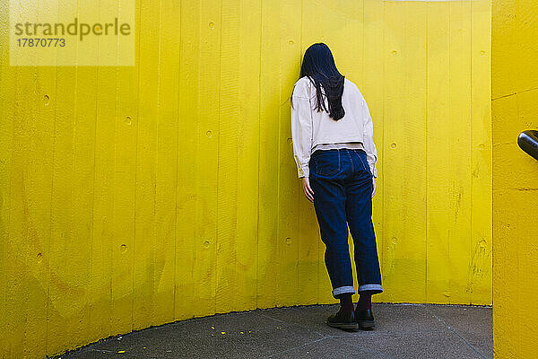 Deprimierte junge Frau lehnt an gelber Wand