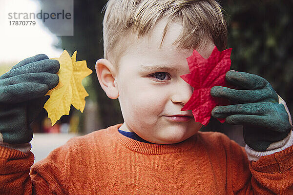 Junge bedeckt Auge mit Herbstblatt