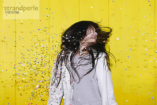 Carefree woman enjoying fallen confetti in front of wall
