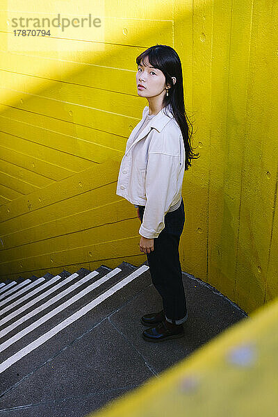 Junge Frau steht vor einer Treppe an einer gelben Wand