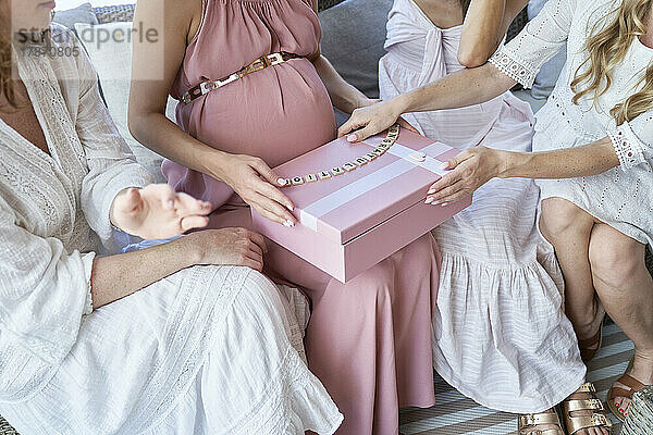 Hände einer schwangeren Frau  die eine Geschenkbox öffnet und mit Freunden sitzt