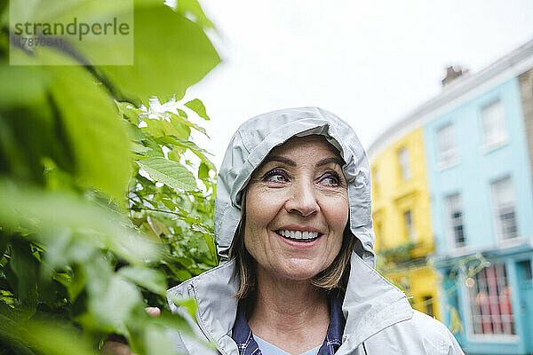 Lächelnde ältere Frau in Windjacke neben Pflanzen