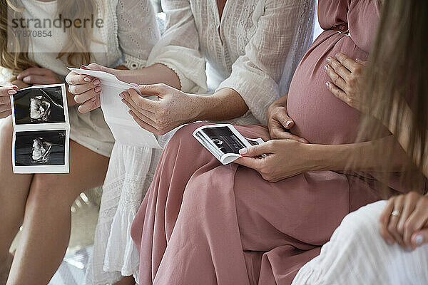 Hände einer schwangeren Frau mit Freunden  die bei der Babyparty das Ergebnis eines Ultraschallscans halten