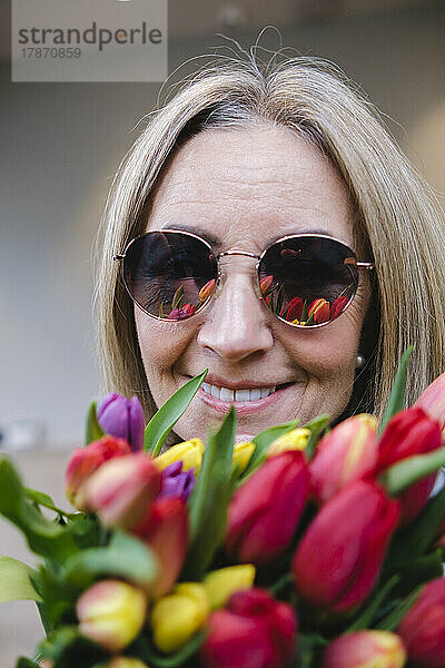 Lächelnde ältere Frau mit Blumen und Sonnenbrille