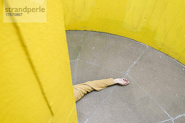 Hand eines bewusstlosen Mannes auf dem Boden an einer gelben Wand