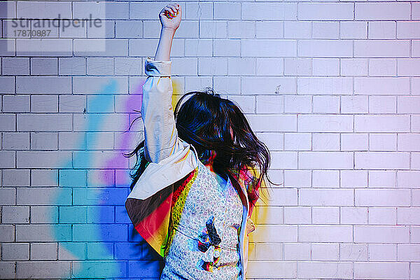 Junge Frau mit erhobenem Arm tanzt vor der Wand