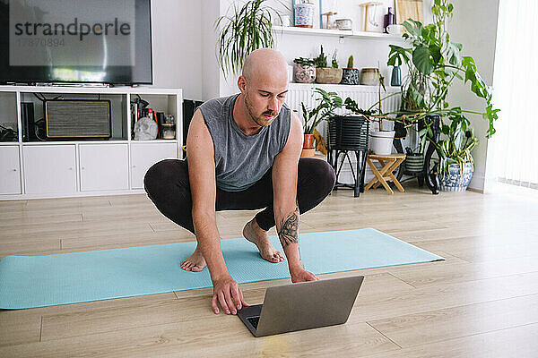 Mann benutzt Laptop auf Trainingsmatte zu Hause