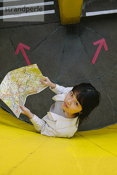 Young woman holding map standing by wall with arrow symbols on floor