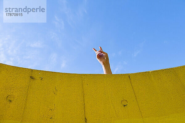 Hand einer jungen Frau zeigt Friedensgeste vor blauem Himmel