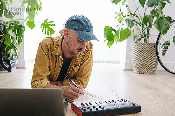Mann mit Klavier und Laptop schreibt zu Hause in ein Buch