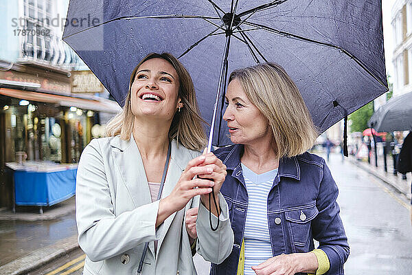 Mutter und Tochter gehen gemeinsam mit Regenschirm auf der Straße spazieren