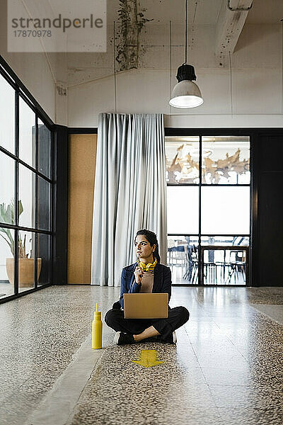 Nachdenkliche junge Geschäftsfrau sitzt im Büro auf dem Boden