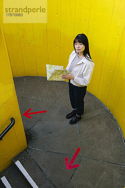 Woman holding map standing on staircase in front of wall
