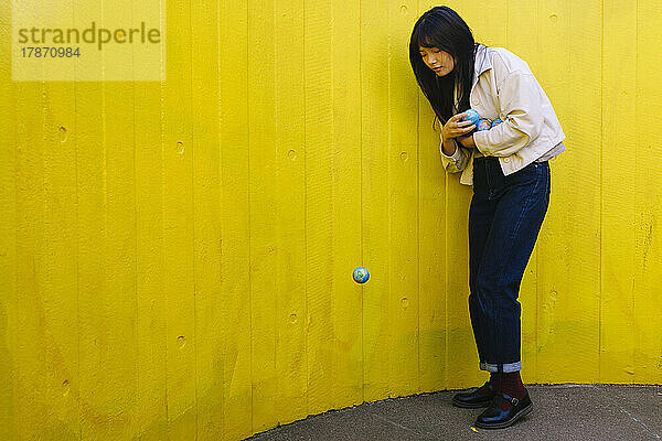 Junge Frau blickt vor gelber Wand auf den umgefallenen Globus