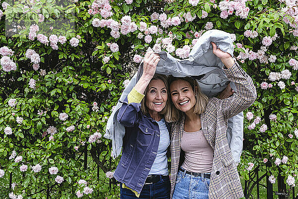 Lächelnde Mutter und Tochter unter Windjacke vor Blumen