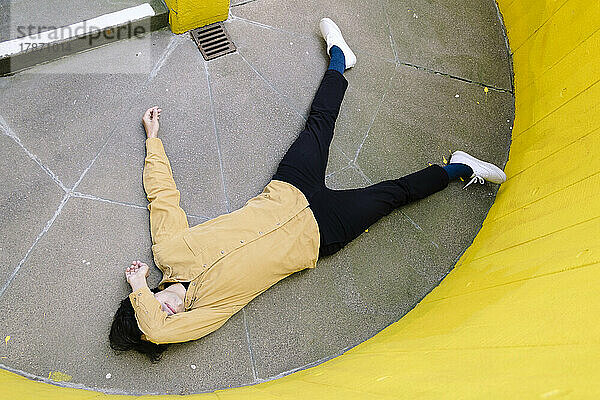 Mann bedeckt die Augen mit der Hand und liegt bewusstlos auf dem Boden neben einer gelben Wand