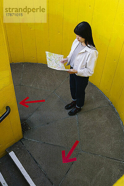 Junge Frau blickt auf die Karte und steht neben Pfeilsymbolen