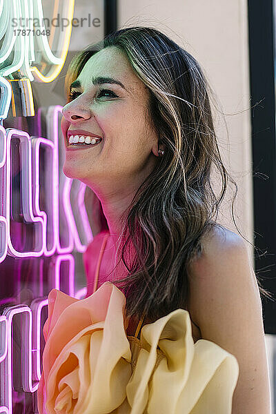 Cheerful young woman by illuminated neon lights