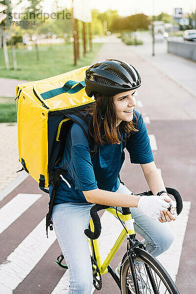 Lächelnde junge Lieferfrau  die auf dem Fahrrad sitzt