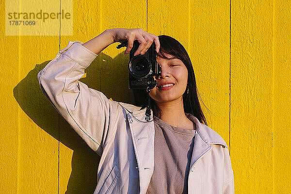 Lächelnde junge Frau fotografiert vor gelber Wand