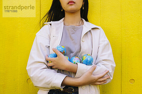 Young woman with globes standing in front of yellow wall