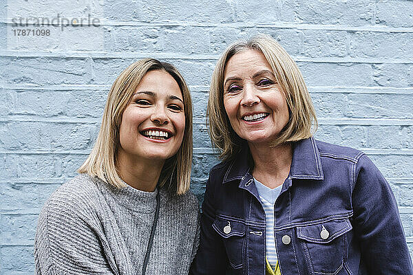 Lächelnde blonde Mutter und Tochter vor blauer Wand