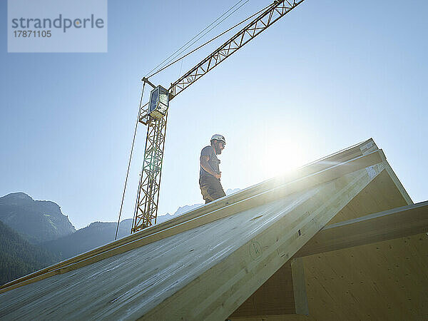 Zimmermann steht auf dem Dach einer Baustelle unter klarem Himmel