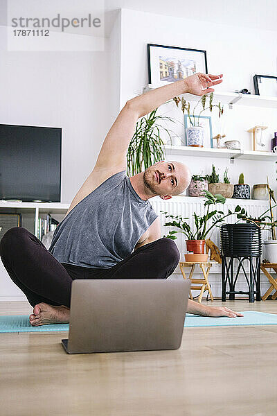 Mann mit erhobener Hand praktiziert Yoga auf einer Trainingsmatte zu Hause