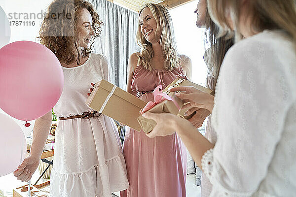 Lächelnde Freunde  die der schwangeren Frau ein Geschenk machen