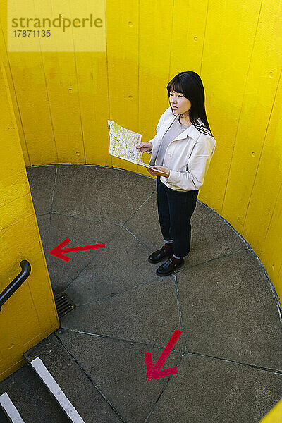 Verwirrte Frau hält Karte vor der Wand