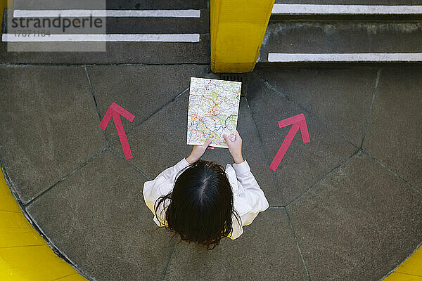 Young woman reading map standing amidst arrow symbols