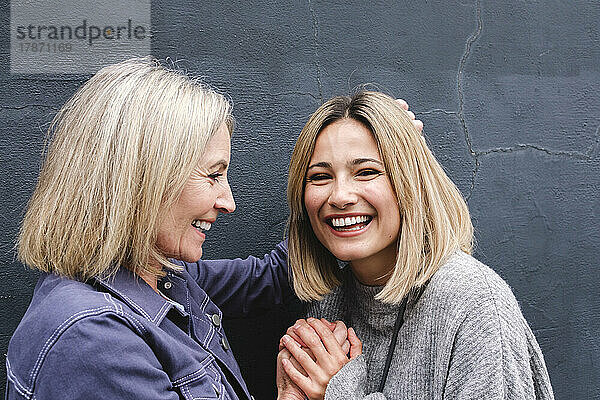 Glückliche blonde Mutter und Tochter halten Händchen vor der Wand
