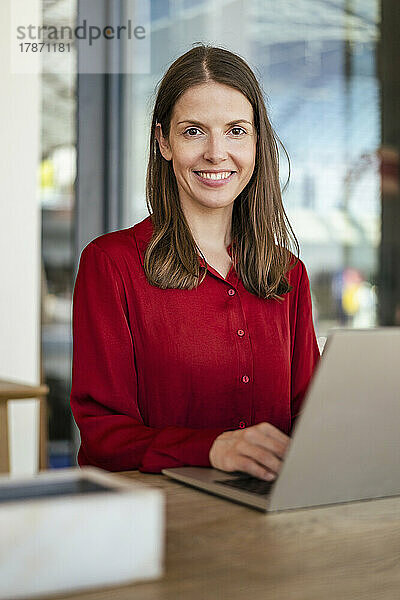 Lächelnde Geschäftsfrau mit Laptop am Schreibtisch im Büro
