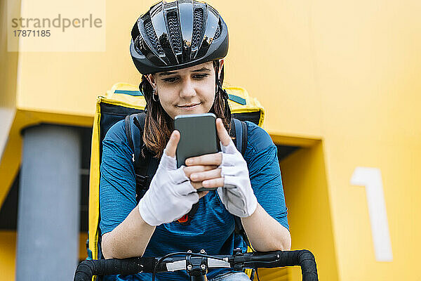 Lächelnde Zustellerin mit Helm und Textnachrichten per Smartphone