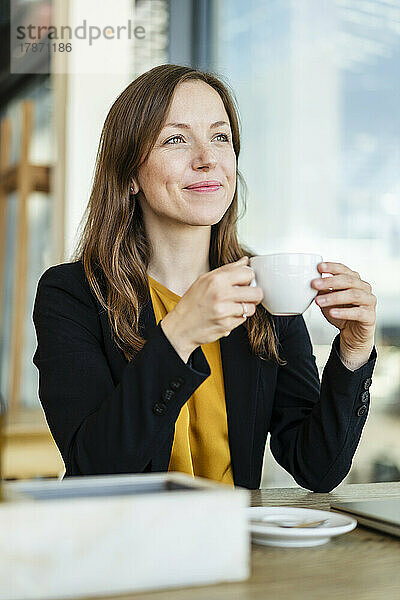 Lächelnde Geschäftsfrau hält Tasse im Café