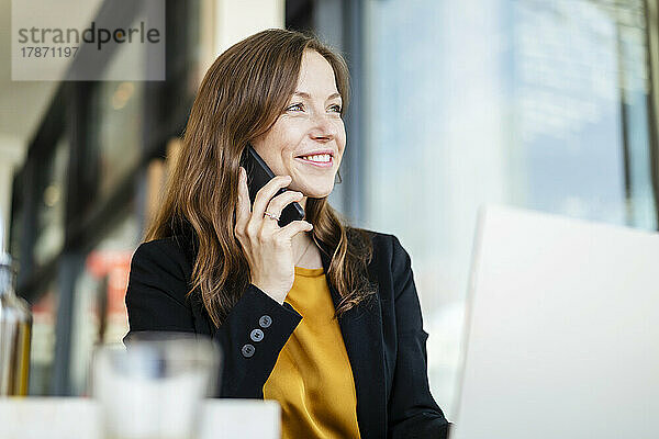 Lächelnde Geschäftsfrau  die im Café mit dem Smartphone spricht