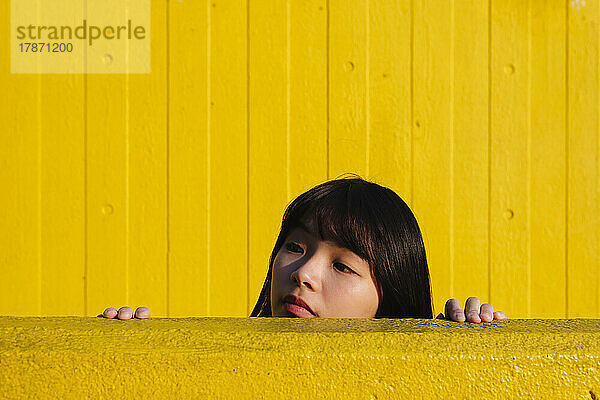 Junge Frau späht von der gelben Wand